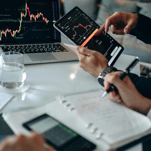 Business professionals reviewing financial charts on digital devices in a modern office setting.