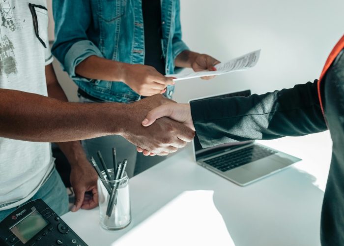 Two business professionals engaging in a handshake agreement in a modern office environment with documents present.